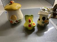 Lot of mushroom jar, chicken salt and pepper holder, and mushroom milk pitcher displayed on a table.
