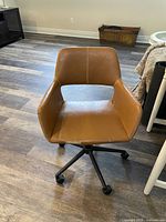 Full view of brown office chair with adjustable height and black five-wheel base on wood floor.