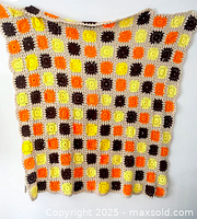 Full view of the orange, yellow, brown, and beige checkered crocheted afghan hanging against a white background, showing the pattern and size.