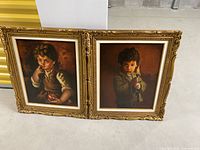 Pair of framed paintings side by side on floor. Each painting depicts a young boy in warm-toned background with gilt ornate frames.