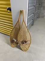 Pair of resin snowshoes leaning against a wall near storage unit doors, showing overall condition and shape.