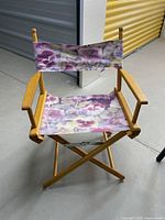 Full view of foldable wooden director's chair with purple floral fabric seat and backrest.