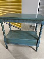Front view of blue wooden side table showing turned legs, lower shelf, and fluted apron detail.