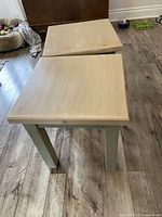 Pair of refinished wooden side tables on a wood floor, showing square light wood tops and grey legs
