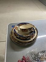 Stack of six pieces of fine china including cup, saucer, and plates showing blue and orange patterned rims with gold accents