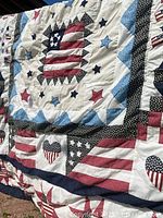 Close-up angled view of quilt displaying central square with American flag and surrounding star patterns in red, white, blue, and black polka dot fabric.