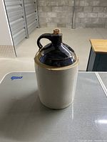 Front view of vintage stoneware crock jug showing cream colored body and dark brown glazed top with handle and cork stopper