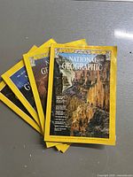 Four vintage National Geographic magazines stacked, showing covers and iconic yellow borders