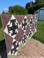 Full view of the quilt hung outside, showing the large geometric black and white block pattern with brown background.
