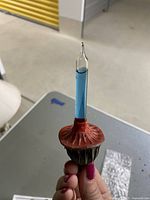 Close-up photo of a vintage rocket bubble Christmas light held by a hand showing the blue liquid inside a narrow glass tube with a red-orange plastic base.