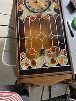 Full view of stained glass clock showing plug-in cord and wood frame with decorative stained glass pattern.