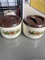 Photo showing two vintage Sterlite Tupperware containers with brown lids and floral pattern on the side.