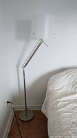 Full view of floor lamp beside bed showing stand, adjustable arm, white drum shade