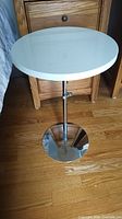 Full view of side table showing white top, chrome shaft, chrome base