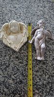 Plaster relief cherub and plastic cherub beside tape measure