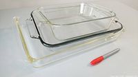 Three nested clear glass baking dishes beside a marker for scale