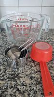 Pyrex 8-cup measuring cup with smaller Pyrex inside, stainless steel measuring cups and red mesh cup on countertop