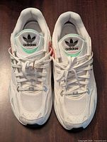 Top view of Adidas shoes showing white mesh and synthetic upper with green and coral accents, black Adidas trefoil logo on tongue.