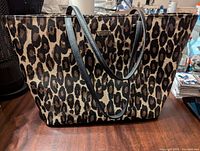 Front view of the large leopard print vinyl tote with black leather handles on wooden surface.