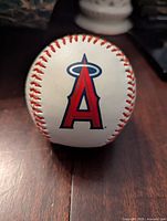 Baseball with Los Angeles Angels large red 'A' logo with blue halo on white leather and red stitching.