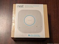 Front view of unopened Nest Protect smoke and carbon monoxide detector packaging sealed in store shrinkwrap.