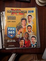 Closed binder with Panini Adrenalyn XL 2018 FIFA 365 official trading card game board visible on cover featuring soccer players.
