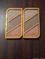 Two unopened black and gold Rimmel Kate makeup palettes lying flat, showing front packaging with highlighter, contour powder, and blush powder sections