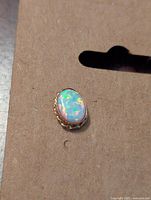 Close-up of single oval white opal earring showing colorful play of color in stone and gold-tone frame