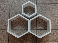 Three white hexagon-shaped wall shelves grouped together on tiled floor, showing front and interior of the shelves.