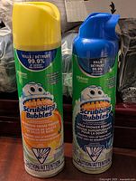 Front view of two aerosol cans of Johnson Scrubbing Bubbles cleaners, one yellow capped bathroom cleaner and one blue capped shower foam.