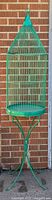 Full view of the green metal vintage birdcage with attached stand against a brick wall background.
