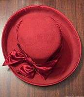 Top view of red felt hat showing wide brim and large satin bow decoration on side