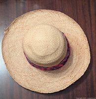 Top view of the natural-colored woven straw sunhat with the pink and purple scarf attached around the crown.