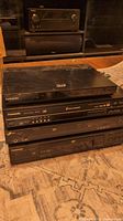 Stack of one Samsung 3D Blu-ray player and three DVD players with a receiver in background.
