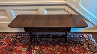 Antique wooden coffee table with both drop leaf sides extended, showing full length and curved legs on a patterned rug.