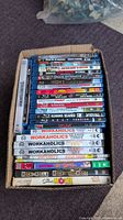 Top view of a box containing assorted Blu-Ray and DVD movies and TV shows, including Duck Dynasty, multiple seasons of Workaholics, RocknRolla Blu-Ray, and more.