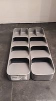 Two gray plastic cutlery organizers side by side in a vertical position showing multiple compartments.