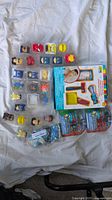 Top view of 26 assorted Mash'ems collectible figures and Peppa Pig keychains arranged on a white sheet next to a boxed kids shaving kit.