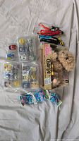 Top view of multiple kids toys including a boxed FurReal Scruffies Charlie robot dog, Peppa Pig keychains, ladybug figures, and 20 sealed Mashems packs.