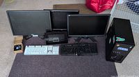 Wide photo showing full lot on floor including 3 monitors, 2 Acer and 1 Dell, 2 Razer keyboards, digital picture frame, USB fan, and black computer case with stickers.