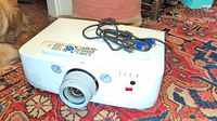 Front view of NEC PA500U projector with lens, remote control on top, and VGA cable coiled up