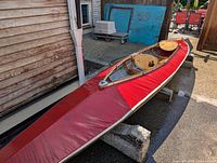 Full view of red double kayak outdoors on stands next to a building showing overall condition and design.