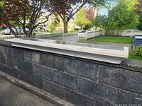 Side and top view of solid wood painted white fireplace mantle resting on concrete wall outside.