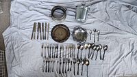 Full lot laid out on cloth showing all components: knives, forks, spoons, serving plate, ornate basket serving dish, ice bucket with stand and tongs.