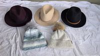 Five women's hats laid out on white background, showing three wide-brimmed hats and two touques.