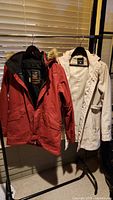 Two jackets hanging on a rack: red Burton ski jacket and white Marika raincoat.