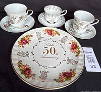 Three tea cups and saucers displayed with decorative anniversary plate.