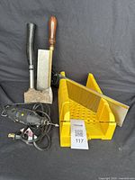 Photo showing the Dremel rotary tool, metal hatchet with black handle, wooden handled chisel, and yellow plastic miter box with backsaw blade