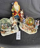 Overall view of the lot showing the Santa figurine and two musical snow globes on sculpted snowy bases.