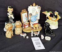 Group view of all collectibles including Rockwell painter, graduate boy, child figurines, hummingbird music box, black dog, and miniature dollhouse items